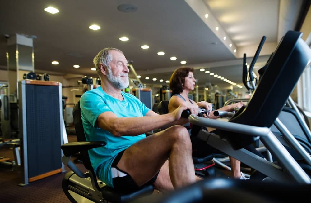 A pair of elderly couple exercising on recumbent exercise bikes in the gym