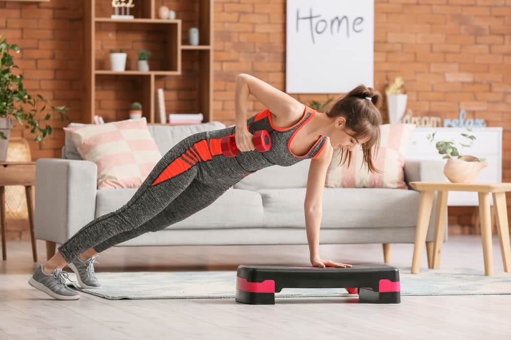 Woman performing renegade row stabilising with one hand on the step platform