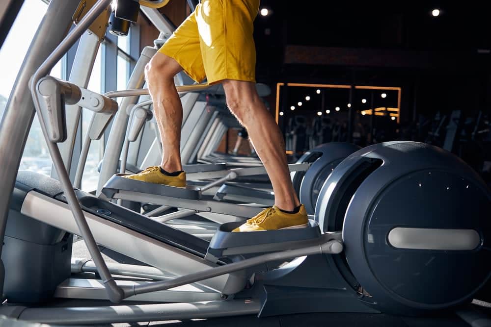 A person wearing a pair of yellow shorts exercising on an elliptical trainer in the gym