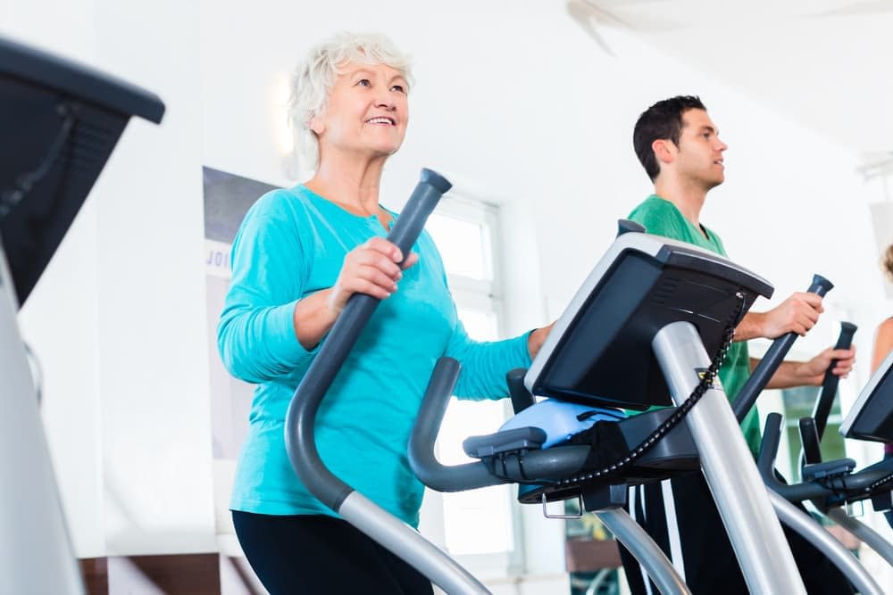 Elderly woman exercising on an elliptical cross trainer in the gym