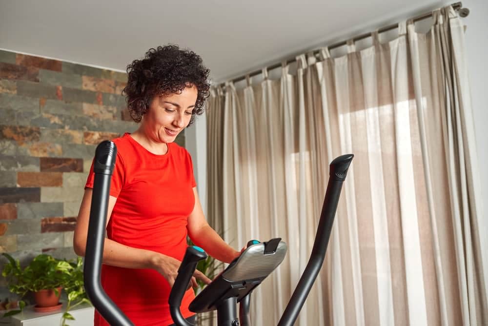 Woman wearing a red top adjusting the settings of her elliptical cross trainer in her living room