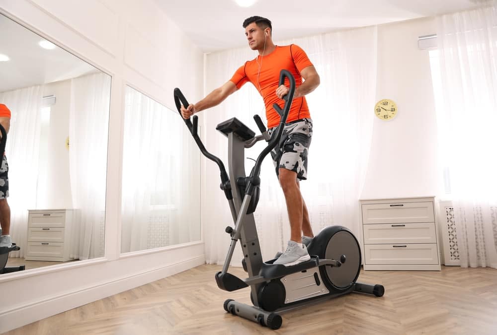 Young man listening to music while exercising on his elliptical trainer at home